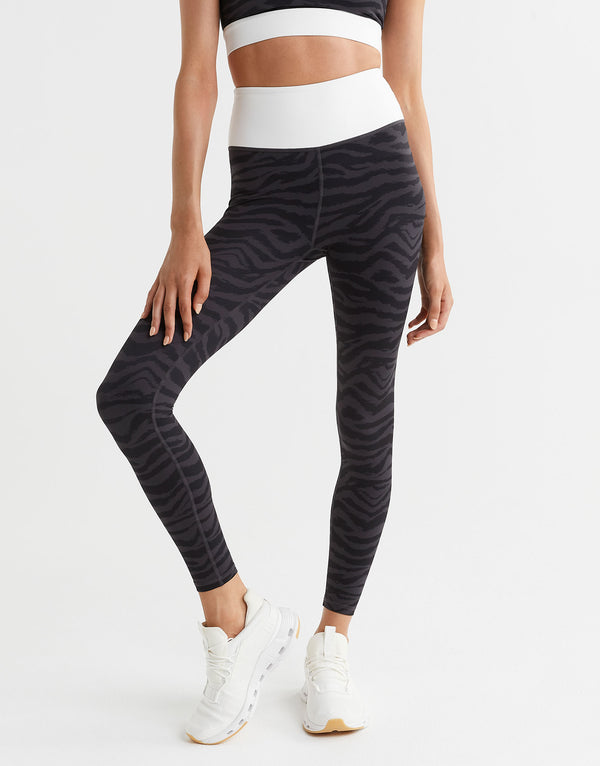 Person wearing black zebra-striped leggings and white sneakers on a light gray background