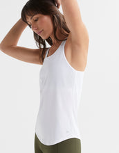 Woman wearing a white tank top and green pants on a light background