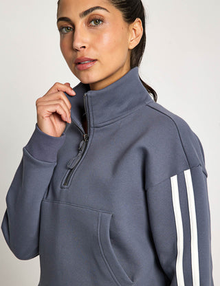 Woman wearing a gray half-zip sweatshirt with white stripes on a plain background