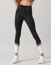 Person wearing black leggings with white accents and white sneakers on a gray background