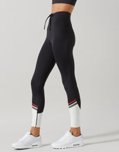 Black leggings with white accents and red and green stripes worn by a person on a light gray background