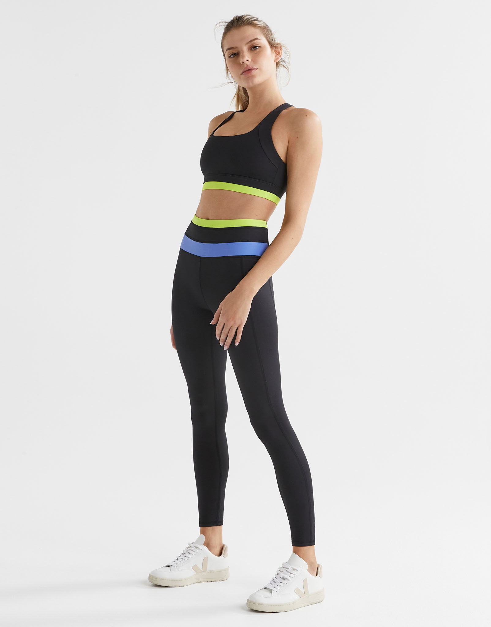 A woman wearing a black sports bra with blue and yellow accents on the under-bust band and cross-back design with matching leggings.