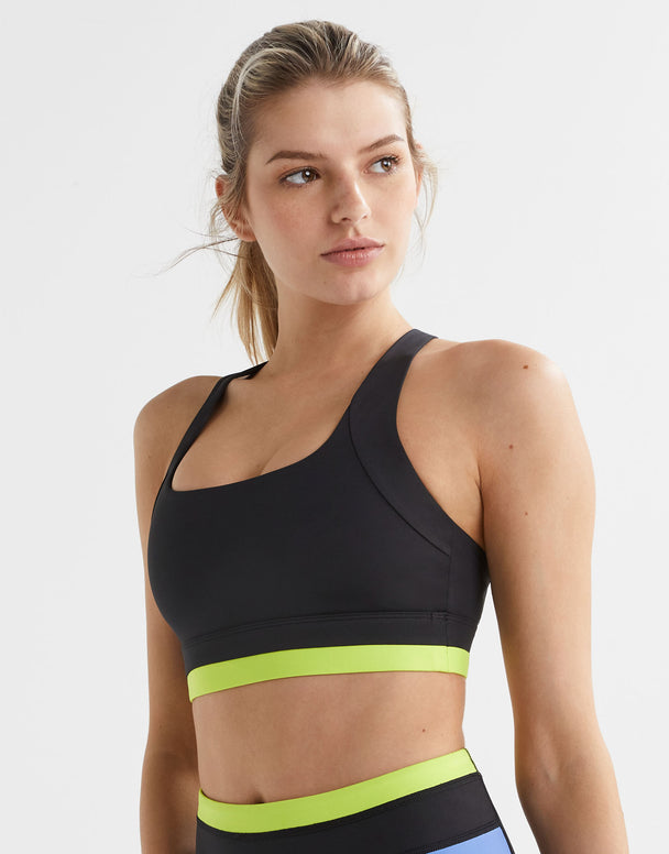 A woman wearing a black sports bra with blue and yellow accents on the under-bust band and cross-back design.