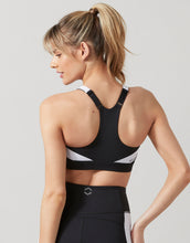Woman wearing a black sports bra with white accents on a light gray background