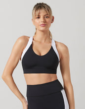 Woman wearing a black sports bra with white straps on a gray background