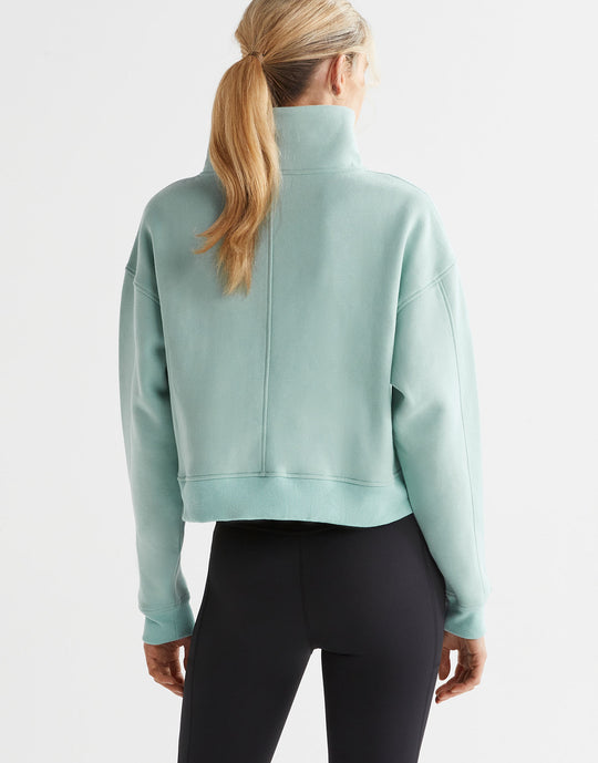 A model wearing a sage green zip up sweater and black leggings.