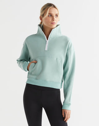 A woman wearing a sage green zip up sweater and black leggings.