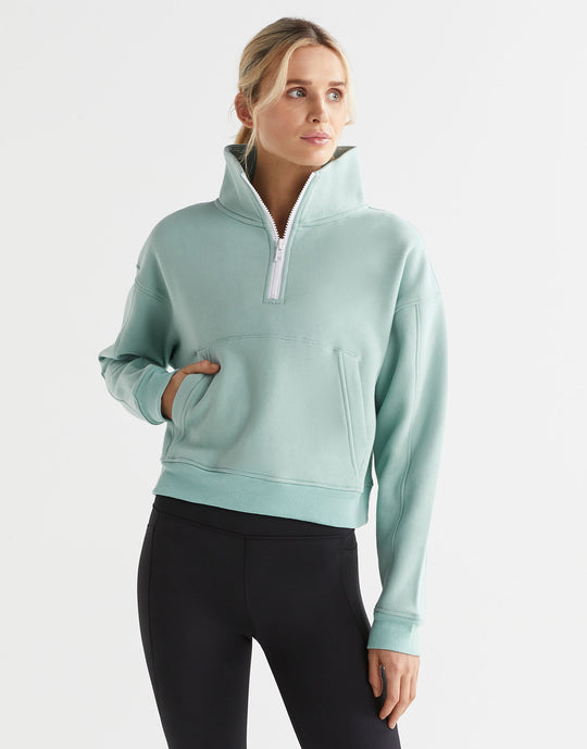 A woman wearing a sage green zip up sweater and black leggings.