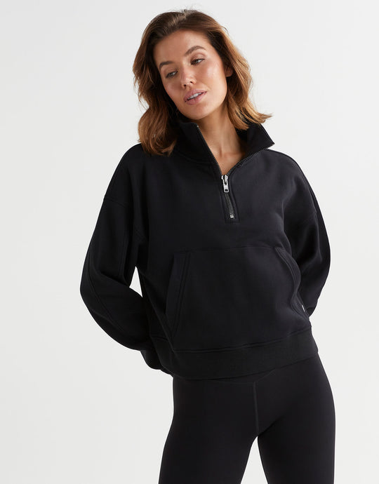 A woman wearing a black quarter zip-up sweater with a relaxed fit and a functional zipper at the front neck opening.