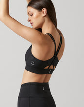 Woman wearing a black sports bra and leggings on a light gray background