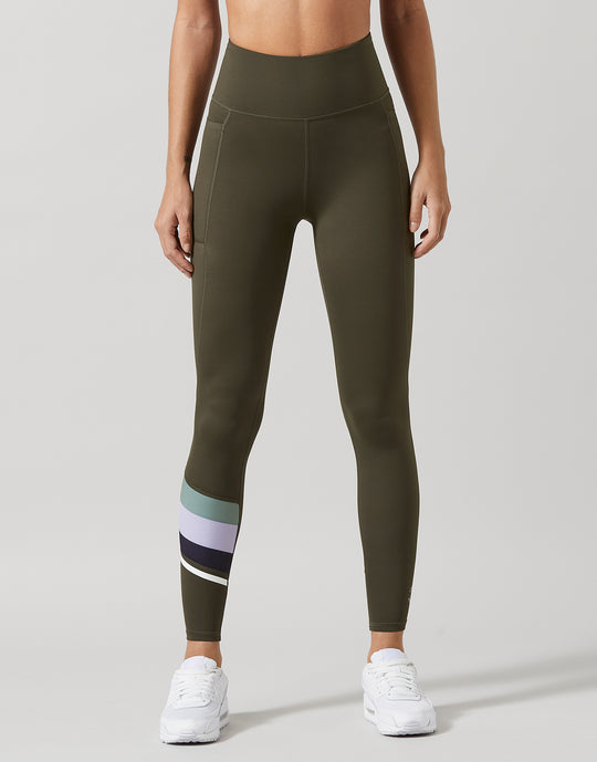 A woman wearing olive green leggings and white runners.