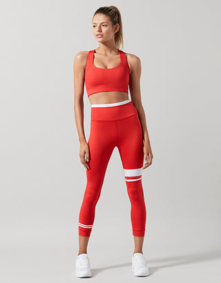 A model wearing a red sports bra and leggings with white trainers.