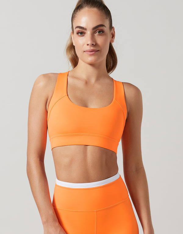 Woman wearing an orange sports bra and leggings on a light gray background