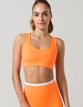 Woman wearing an orange sports bra and leggings on a light gray background