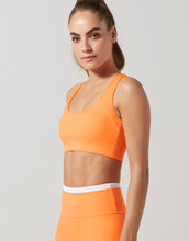 Woman wearing an orange sports bra and leggings on a light gray background