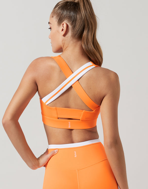 Woman wearing an orange sports bra and leggings on a light gray background