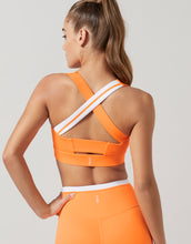 Woman wearing an orange sports bra and leggings on a light gray background