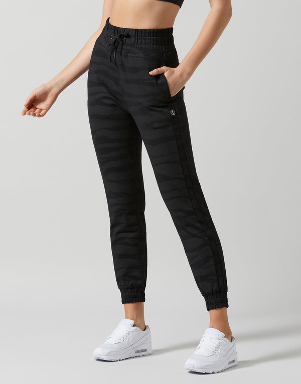 Person wearing black jogger pants and white sneakers on a light gray background