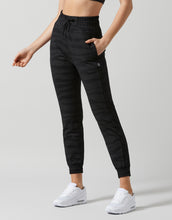 Person wearing black jogger pants and white sneakers on a light gray background