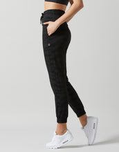Person wearing black jogger pants and white sneakers on a gray background