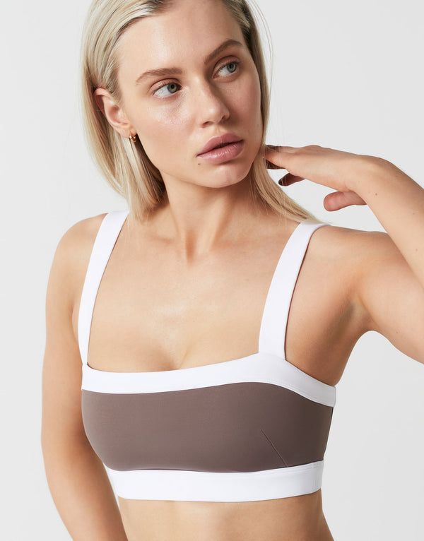 A model wearing a brown and white sports bra on a white background.