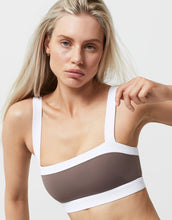 Woman wearing a white sports bra with a brown mesh panel on a light background