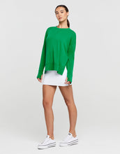 Woman wearing a green sweater and white skirt with white sneakers on a light gray background