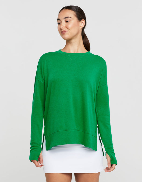 Woman smiling wearing a green sweater and white skirt on a light grey background