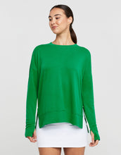 Woman smiling wearing a green sweater and white skirt on a light grey background