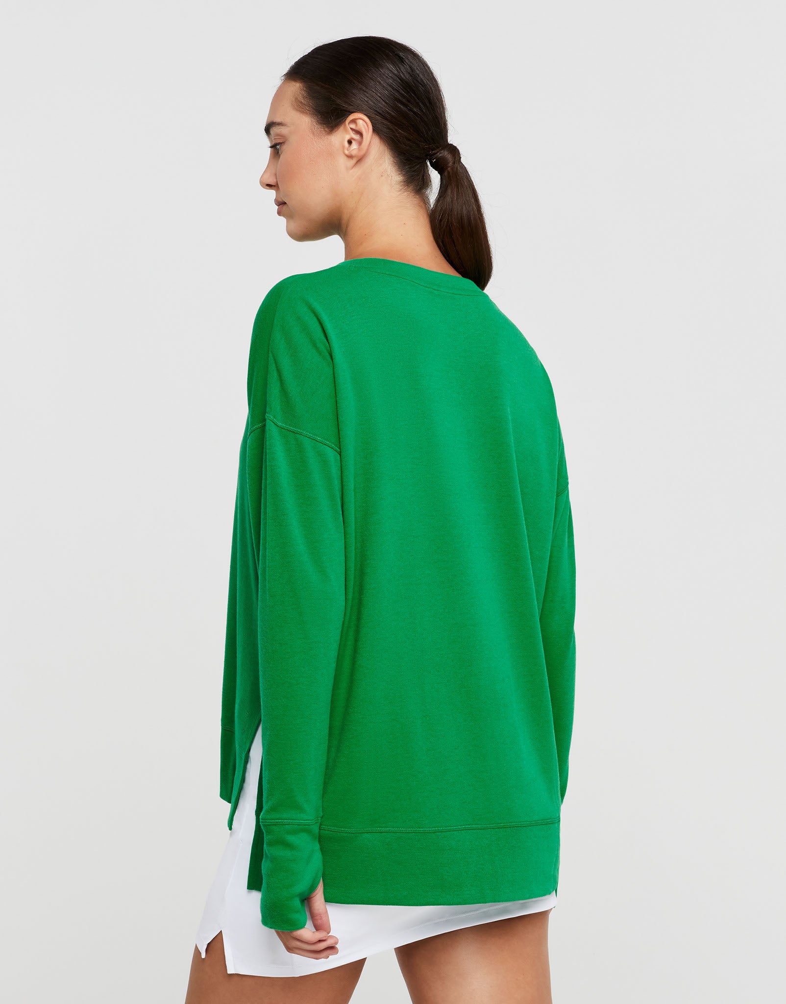 Woman wearing a green sweatshirt and white skirt with a white background