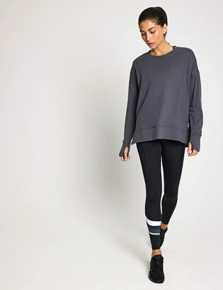 Woman wearing a gray sweatshirt and black leggings with white stripes on a white background