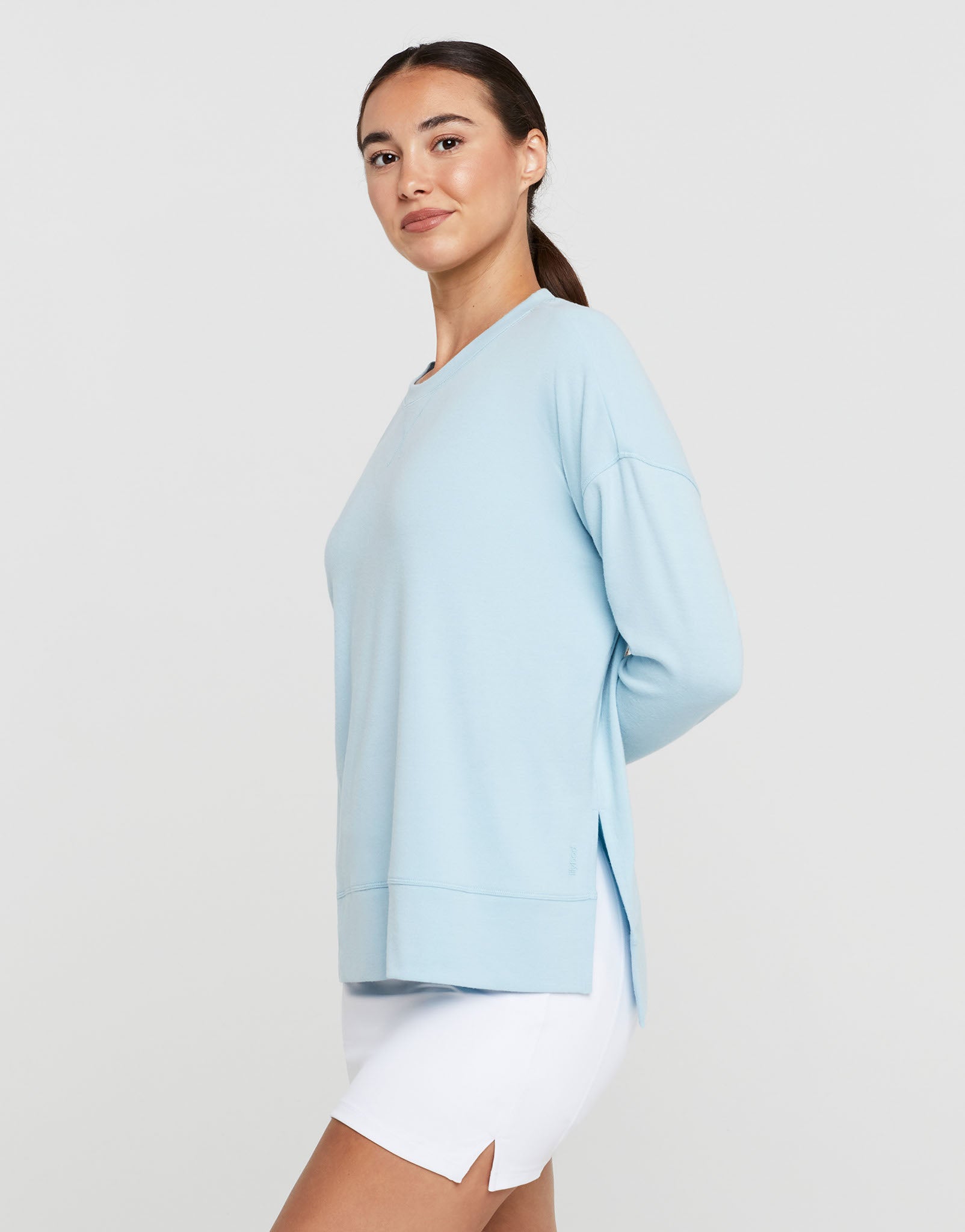 Woman wearing a light blue long-sleeve top and white shorts on a plain background