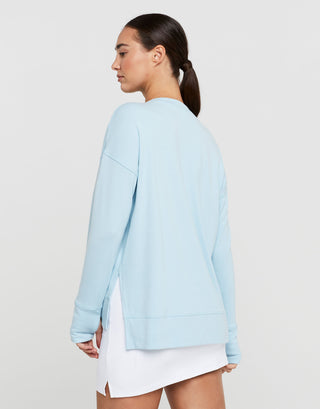 Woman wearing a light blue sweater over a white dress on a plain background