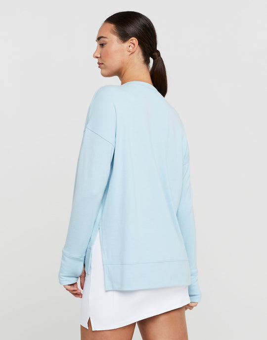 Woman wearing a light blue sweater over a white dress on a plain background