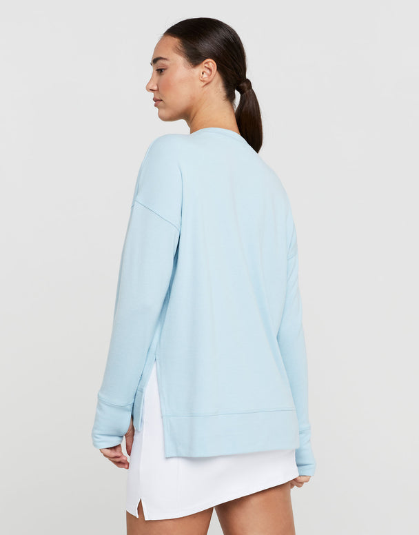 Woman wearing a light blue sweater over a white dress on a plain background