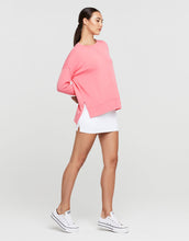 Woman wearing a pink sweatshirt and white shorts on a light gray background