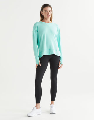 Woman wearing a light blue long-sleeve top and black leggings on a white background