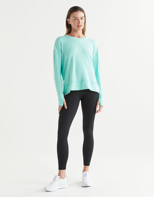 Woman wearing a light blue long-sleeve top and black leggings on a white background