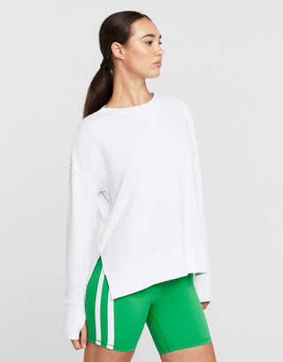 A woman wearing a white long-sleeve sweatshirt and green athletic shorts with white stripes.