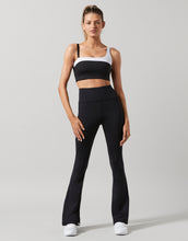 Woman wearing a black and white sports bra and black leggings on a gray background