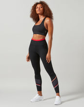Woman wearing a black sports bra and leggings with red accents on a gray background
