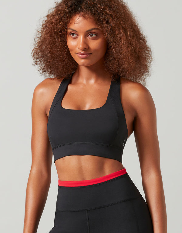 Woman wearing a black sports bra with red trim and black leggings on a gray background