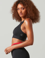 Woman wearing a black sports bra and red underwear on a light gray background