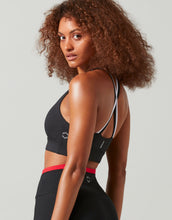 Woman wearing a black sports bra with red trim on a plain background