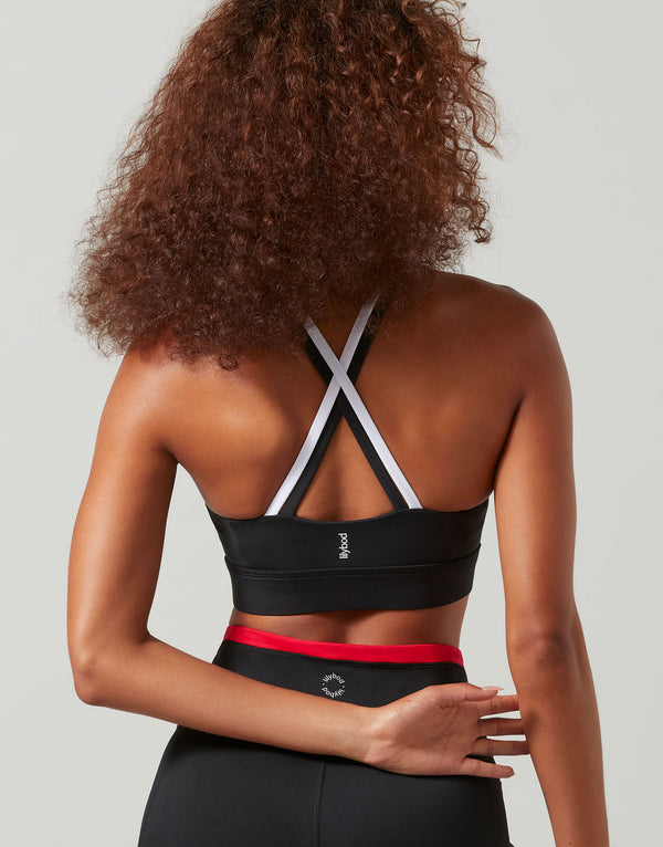 Person wearing a black sports bra with red waistband and white straps on a plain background