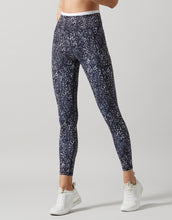 A pair of high-waisted full-length leggings with a hand-sketched safari print, primarily in a dark color, paired with white sneakers.