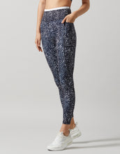 A female in a pair of high-waisted full-length leggings with a hand-sketched safari print, primarily in a dark color, paired with white sneakers.