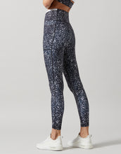 A pair of high-waisted full-length leggings with a hand-sketched safari print, primarily in a dark color, paired with a sports bra and white sneakers.