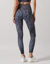 A model in a pair of high-waisted full-length leggings with a hand-sketched safari print, primarily in a dark color, paired with white sneakers.