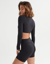 Person wearing a black long-sleeve crop top and high-waisted bike shorts on a white background
